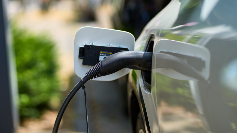 White e-car that is on the charging cable. The electric car is shown from the side where the environmentally conscious vehicle is being charged.