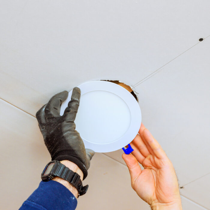 An electrician is carefully placing recessed light fixture into ceiling opening, during home renovation skills.