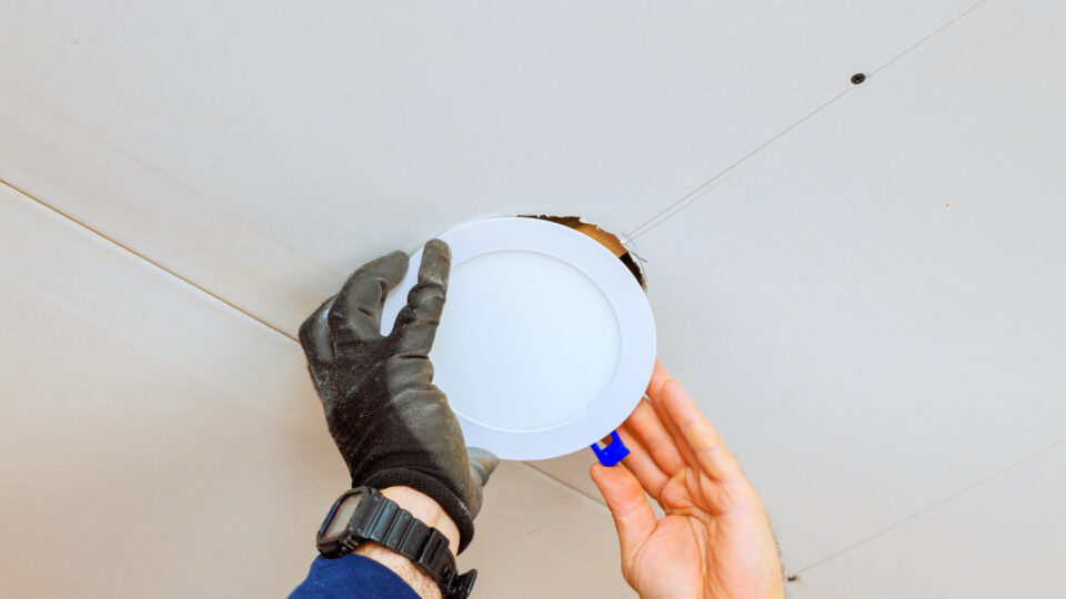 An electrician is carefully placing recessed light fixture into ceiling opening, during home renovation skills.