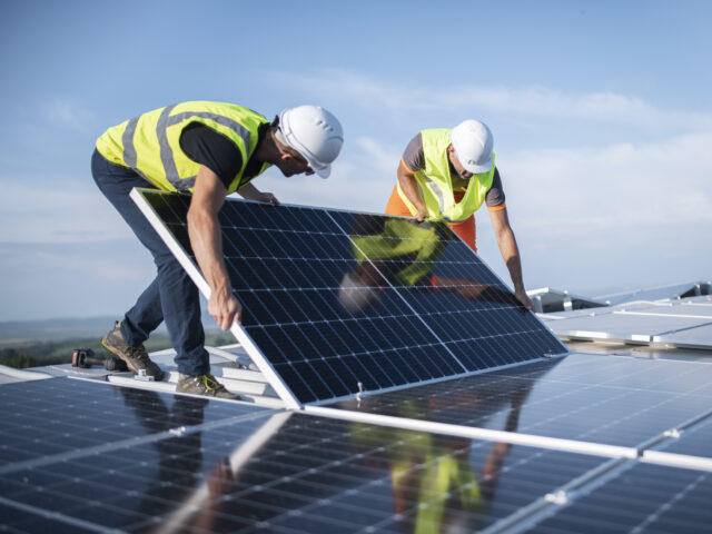 Team of two engineers installing solar panels on roof.